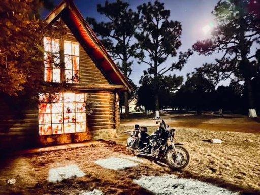 Casa rústica iluminada junto a una motocicleta en un entorno natural.