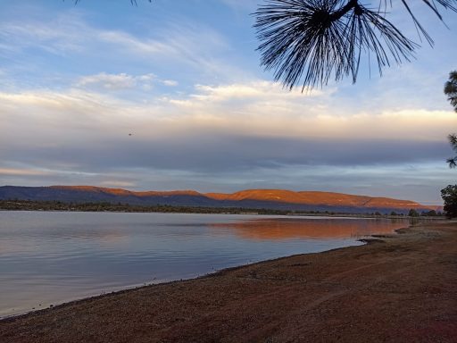 Río sereno al atardecer con montañas reflejadas en el agua y cielo nublado.