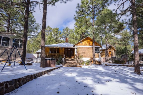 Cabaña de madera en un área boscosa con nieve y árboles alrededor.