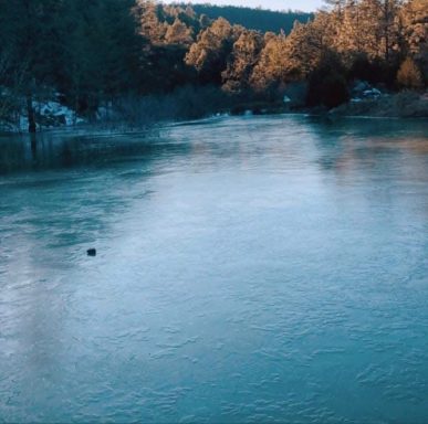 Río sereno rodeado de árboles y montañas, con luz suave del atardecer.